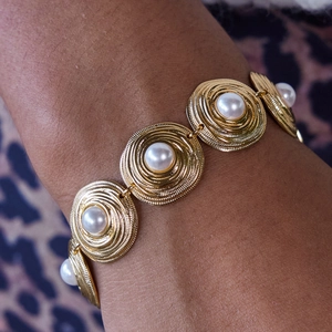 Detailed view of vintage gold spiral bracelet with embedded white pearls on wrist