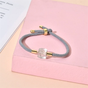 Vue détaillée d'un bracelet tressé gris avec fermoir doré et pendentif en cristal clair