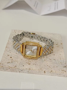 Detailed view of square gold watch with diamond bezel and two-tone metal strap on stone stand