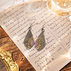 Macro detail of vintage bohemian sunflower teardrop earrings on retro letter paper