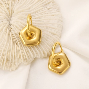 Detailed close-up of golden hexagonal geometric earrings on white coral and silk fabric