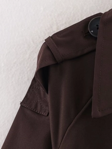 Detail of dark brown trench coat shoulder with buttoned epaulet and twill texture