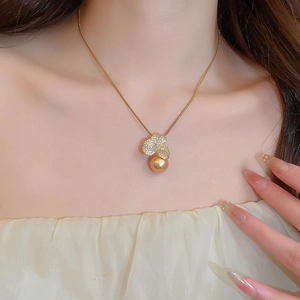 Detailed view of a gold flower pendant with zircon inlay and pearl on a woman's neck
