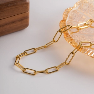 Gros plan du collier à maillons trombone dorés sur un plat en verre ambré chic