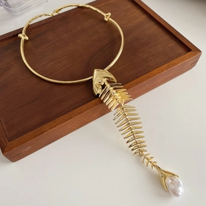 Detailed view of a gold fishbone pendant necklace with pearl on a wooden display tray