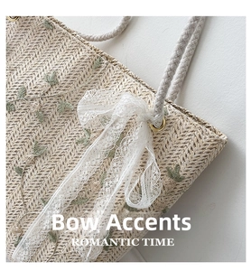 Detailed close-up of straw woven tote featuring green embroidery and white lace bow