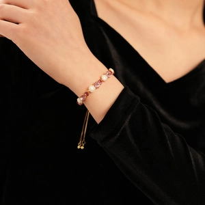 Détail d'un bracelet doré ajustable avec cristaux roses et perles blanches au poignet