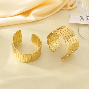 Detail of gold open bangles with wavy texture and leaf design on cream satin fabric