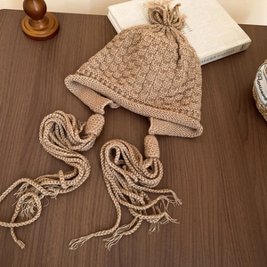 Detail of camel chunky knit hat featuring textured checker patterns and long tassels