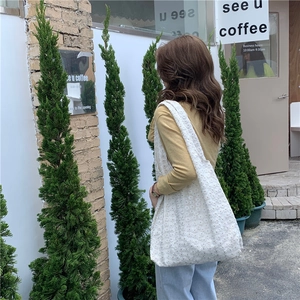 Close-up of a white lace floral tote bag worn by a model in a scenic outdoor setting