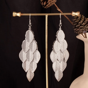 Detail view of silver layered leaf earrings hanging on a display stand with black background