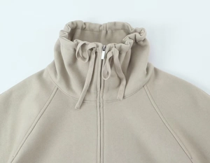 Détail d'un sweat beige avec fermeture éclair, col à cordon réglable et texture douce