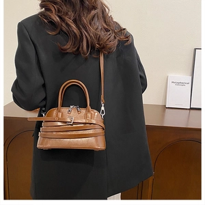 Detailed view of brown shell-style crossbody bag with multi-layer leather strap and metal buckle
