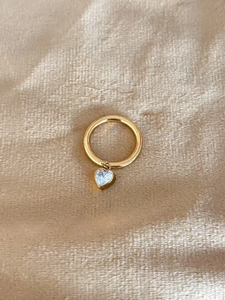Detail of a gold heart charm ring with a clear zircon crystal on textured fabric