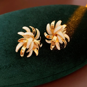 Close-up of vintage gold-plated daisy stud earrings on deep green velvet background