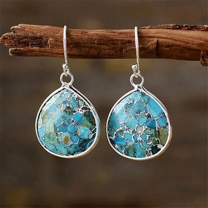 Detailed view of blue teardrop imperial stone earrings hanging on a natural wooden branch