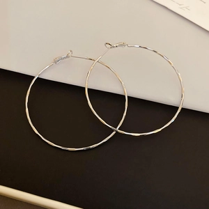 Detailed view of large silver hoop earrings with faceted texture on a split background