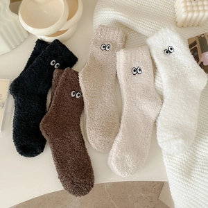 Close-up of cozy coral fleece socks with cute cartoon eye embroidery in soft colors