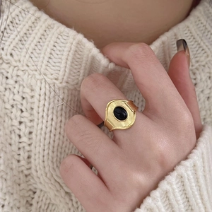 Detailed close-up of a gold-plated ring with oval black onyx worn over a knit sweater
