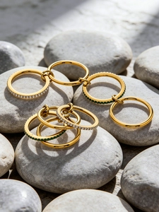Close-up of 18K gold plated stackable rings with zircon and emerald stones on pebbles