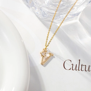 Detail of gold letter V necklace with zircon flower pendant on creative background