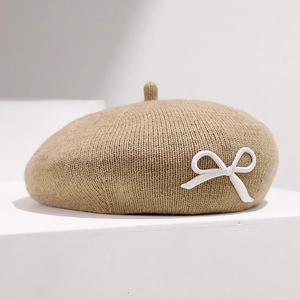 Gros plan d'un béret en tricot camel orné d'un délicat nœud 3D blanc sur le côté