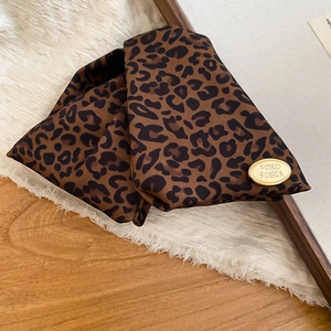 Detail of leopard print triangle hair claw with polished gold metal logo on a wooden table