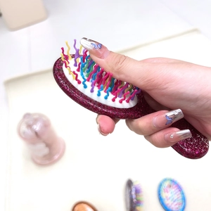Detail of glitter burgundy air cushion brush with colorful wavy bristles held by hand