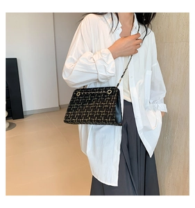 Close-up of black and gold tweed chain bag worn with a white shirt and grey pants