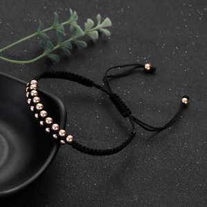 Detailed view of beaded woven bracelet with rose gold beads on a matte black background