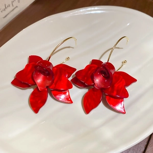 Close-up of red resin flower earrings with gold hooks on a ceramic dish background