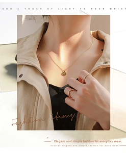 Detail of gold coin letter necklace and minimalist stacking rings set on a model