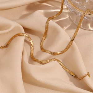 Detailed view of an 18K gold plated herringbone chain on premium champagne silk fabric