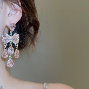 Gros plan de boucles d'oreilles nœud en cristal rose avec pompons portées par un mannequin