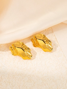 Macro view of gold lava style cheetah stud earrings on beige satin and stone background