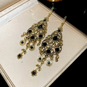 Dettaglio macro di orecchini vintage a nappa con strass neri e motivi floreali traforati