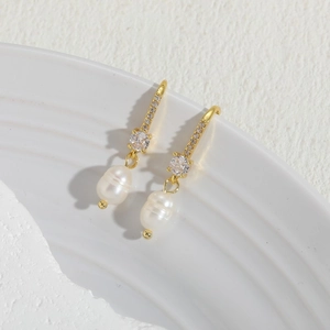 Elegant gold drop earrings with freshwater baroque pearls and zircon stones on a white tray
