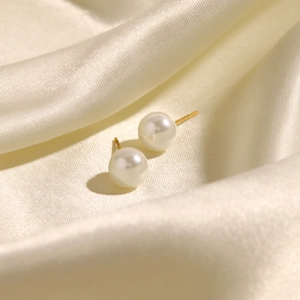 Classic white round pearl earrings on silk background with gold posts for women