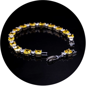 Detail of silver bracelet featuring yellow and white cubic zirconia on black reflective surface
