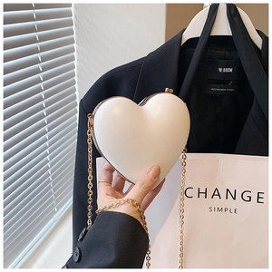 Detail of a beige heart-shaped hardshell clutch with gold metal frame and chain strap