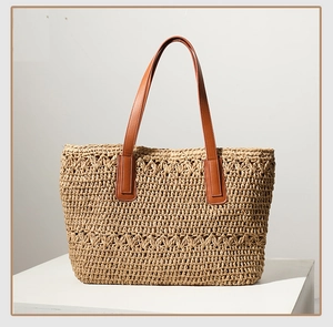 Close-up of khaki straw tote bag featuring brown leather handles and woven texture
