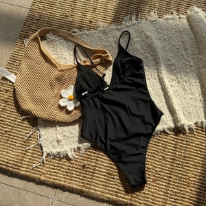 Detail of black one-piece swimsuit with thin straps on rustic summer vacation background