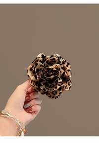 Detailed view of leopard print acrylic flower hair claw clip held by a model
