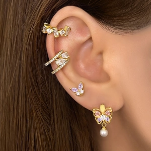 Gros plan de boucles d'oreilles papillon dorées avec zircons colorés et perle sur l'oreille