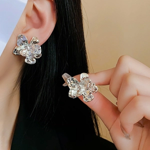 Detail of silver flower earrings with irregular lava texture shown on ear and hand