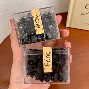 Macro detail of 50 black mini claw clips in a transparent box with a handmade label