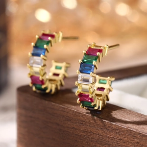 Macro view of C-shaped 925 silver earrings with colorful square zircons on wood