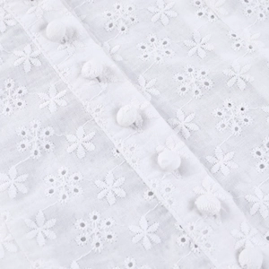 Gros plan sur la broderie en dentelle blanche et les boutons recouverts du haut