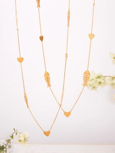 Detailed view of a gold fashion chain featuring heart and fishbone charms on white floral background