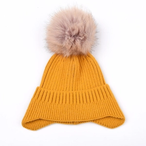 Close-up of thick mustard yellow cable knit beanie with a fluffy pink faux fur pompom